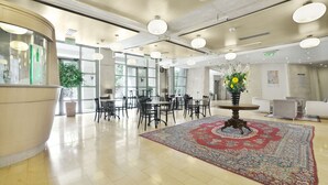 Un vestíbulo espacioso con un gran y ornamentado tapiz, muebles modernos y un arreglo floral central.