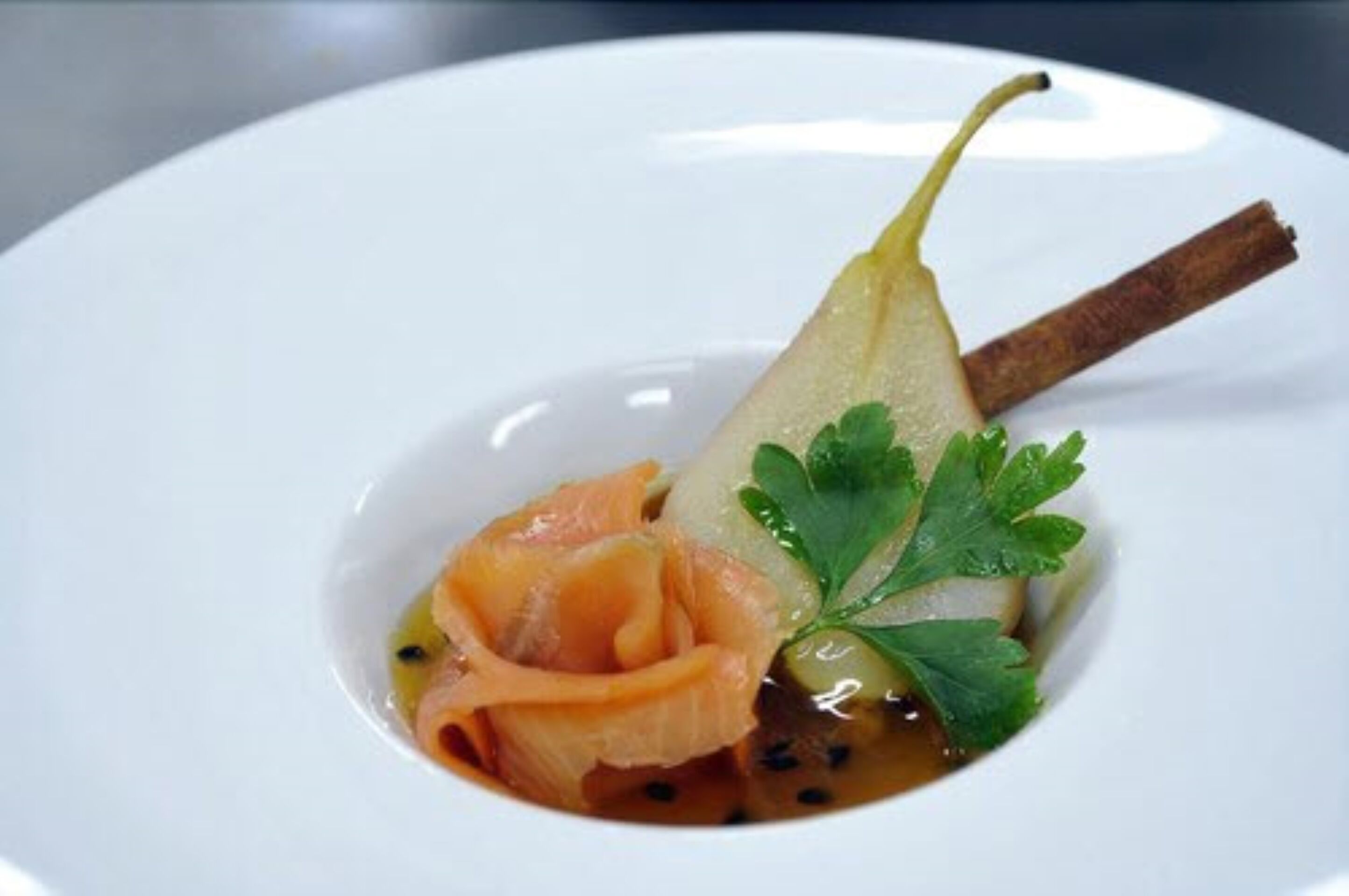 A white plate with a pear, salmon, and a sprig of parsley.