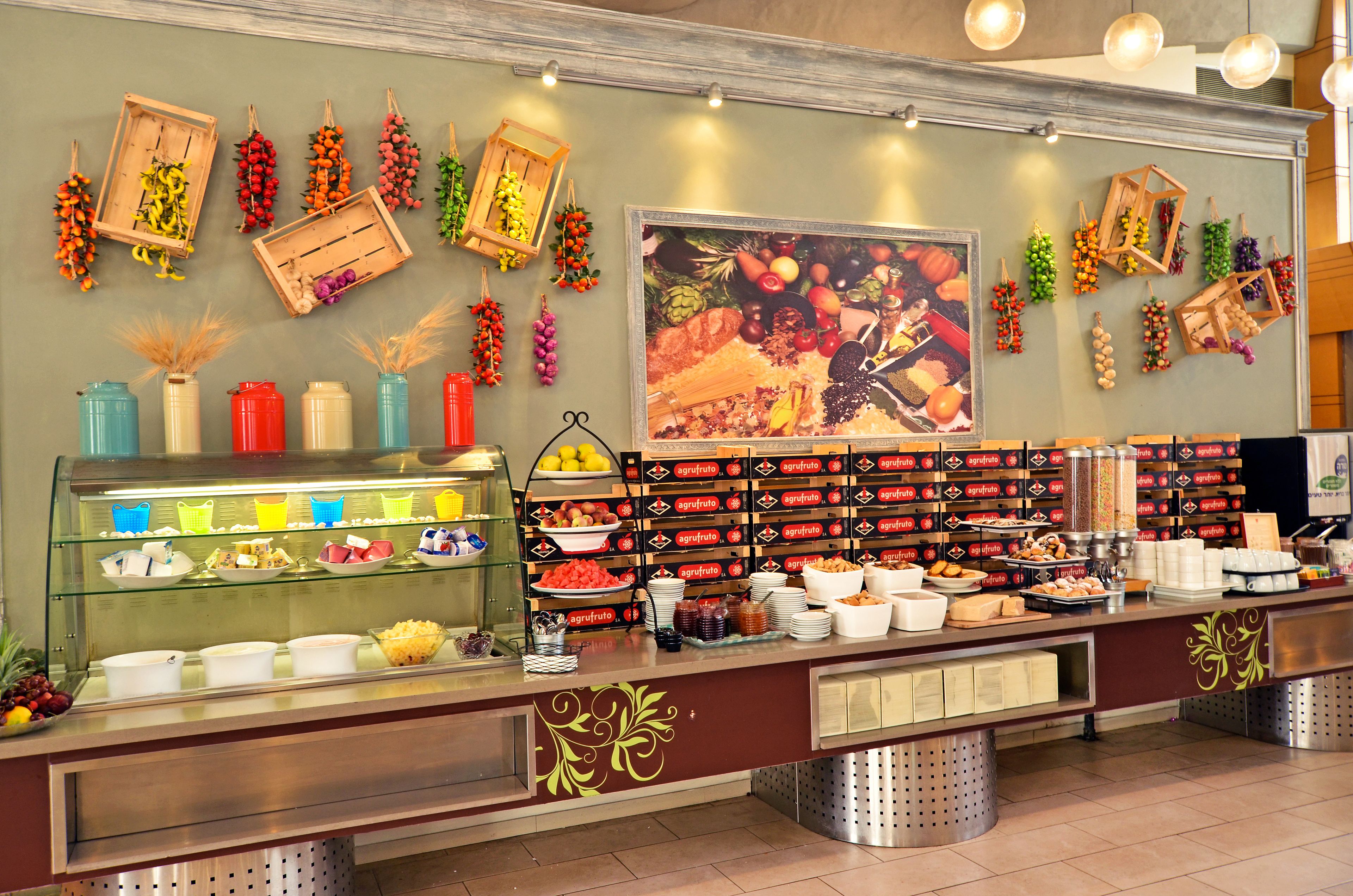 A buffet area with various food items and a wall decorated with hanging fruits and vegetables.