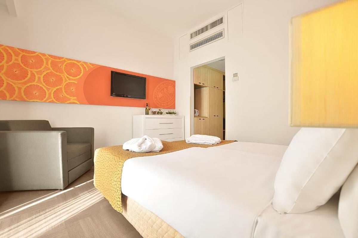 Habitació d'hotel amb llit, sofà, televisió penjada a la paret i armari.