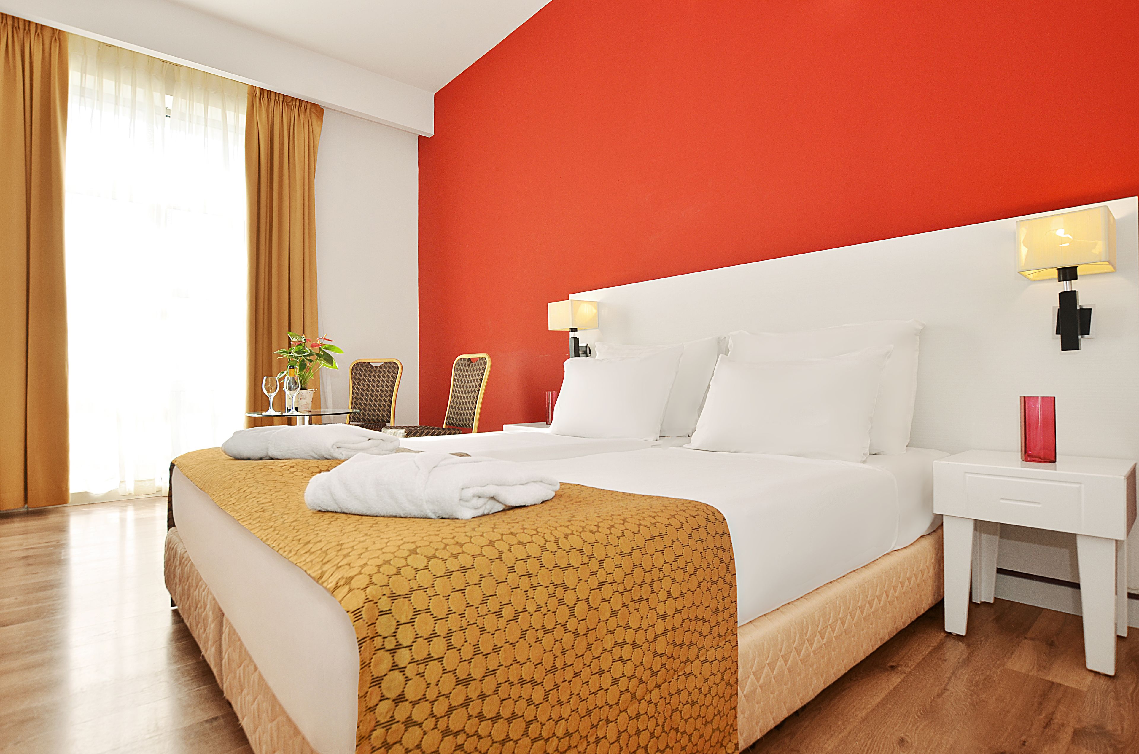 A hotel room with a large bed, a nightstand, a lamp, a chair, and a window with curtains.