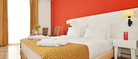 A hotel room with a large bed, a nightstand, a lamp, a chair, and a window with curtains.