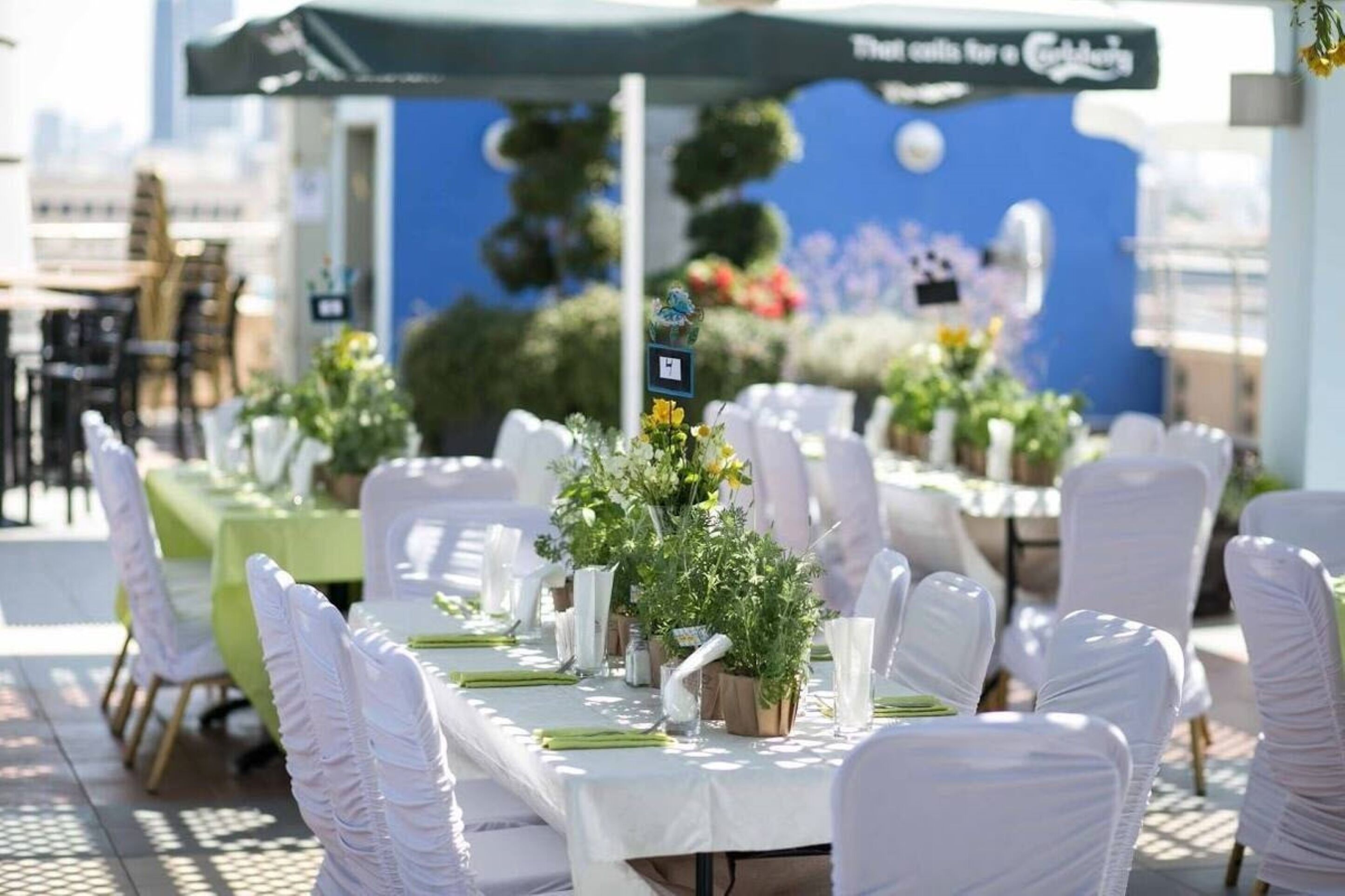 Ein Tisch für eine festliche Outdoor-Veranstaltung, gedeckt mit weißen Tischdecken, weißen Stühlen und floralen Mittelpunkten.