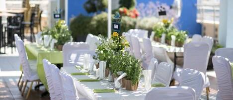 Ein Tisch für eine festliche Outdoor-Veranstaltung, gedeckt mit weißen Tischdecken, weißen Stühlen und floralen Mittelpunkten.