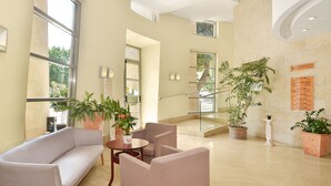 Un amplio hall con un sofá, sillas, una pequeña mesa y plantas en macetas.