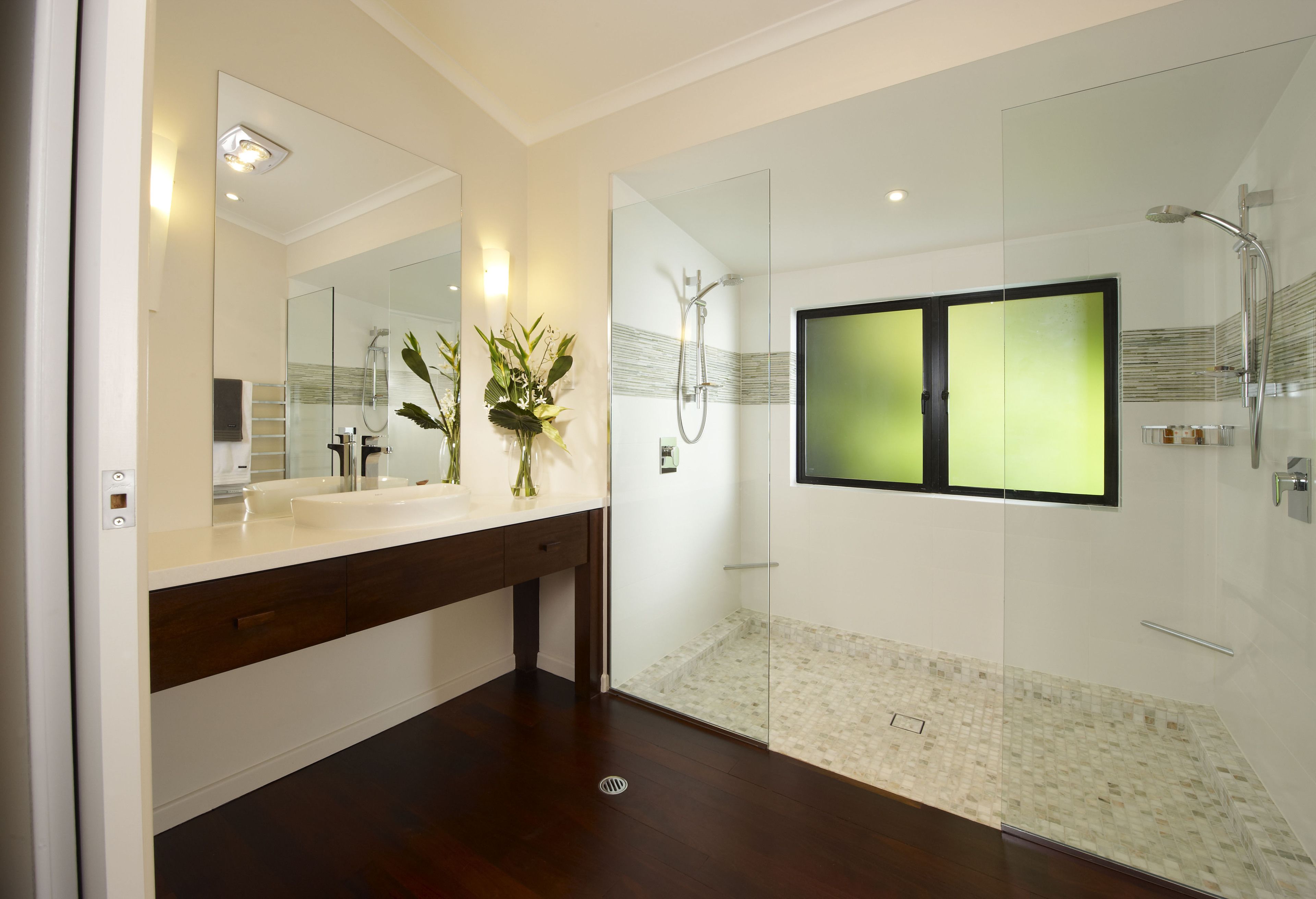 Une salle de bain moderne avec une douche à parois de verre, un grand miroir et un meuble-lavabo blanc.