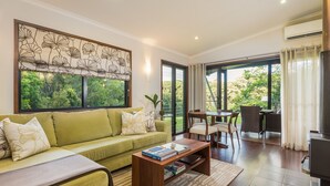 A living room with a green sofa, a wooden coffee table, and a dining area with chairs and a table. - Spicers Tamarind Retreat (Maleny)