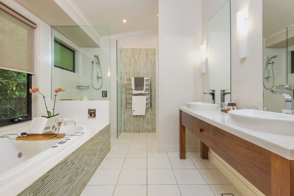 Un baño moderno con una bañera grande, dos lavamanos, un box de ducha de vidrio y un espejo amplio.
