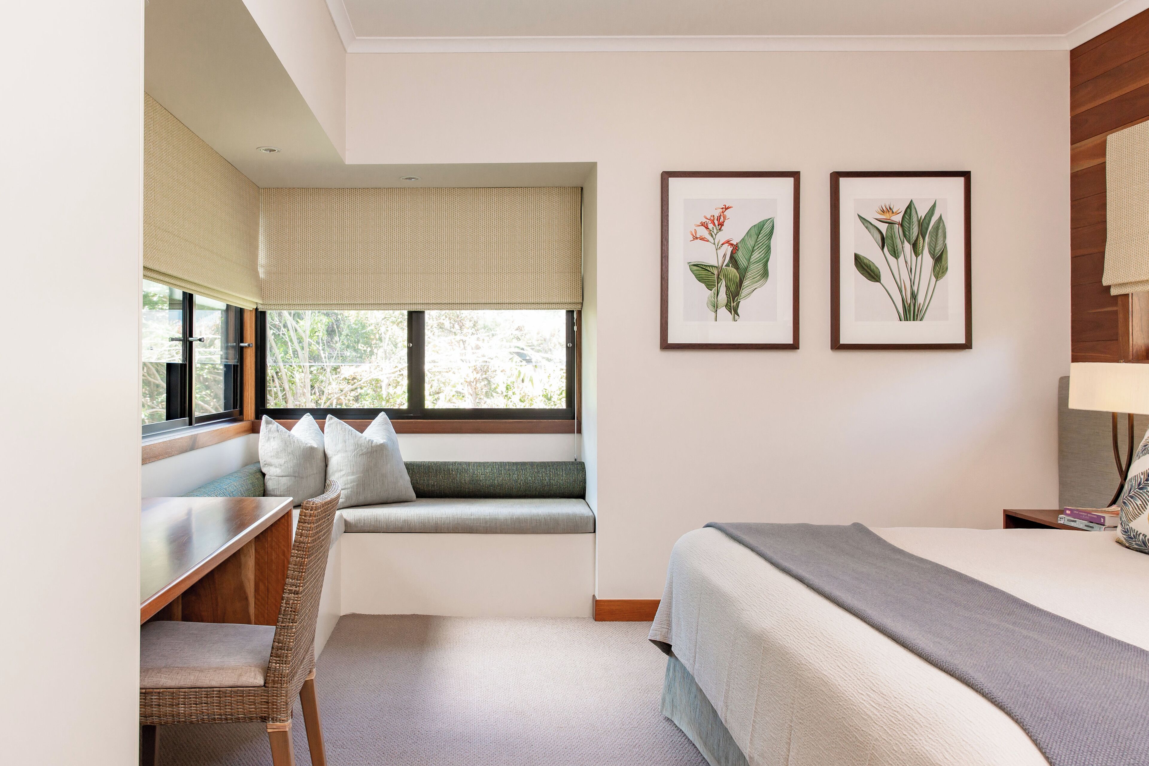 Habitación de hotel con una cama, un escritorio con silla, una ventana con vistas, y dos láminas botánicas enmarcadas en la pared.