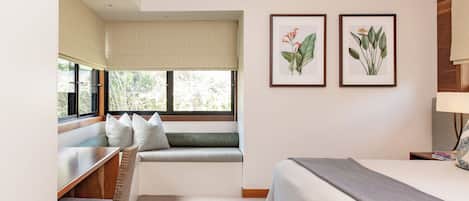 Habitación de hotel con una cama, un escritorio con silla, una ventana con vistas, y dos láminas botánicas enmarcadas en la pared.
