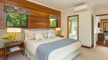 A bedroom with a large bed, wooden headboard, two bedside tables with lamps, a small plant, and a window with a view of trees.