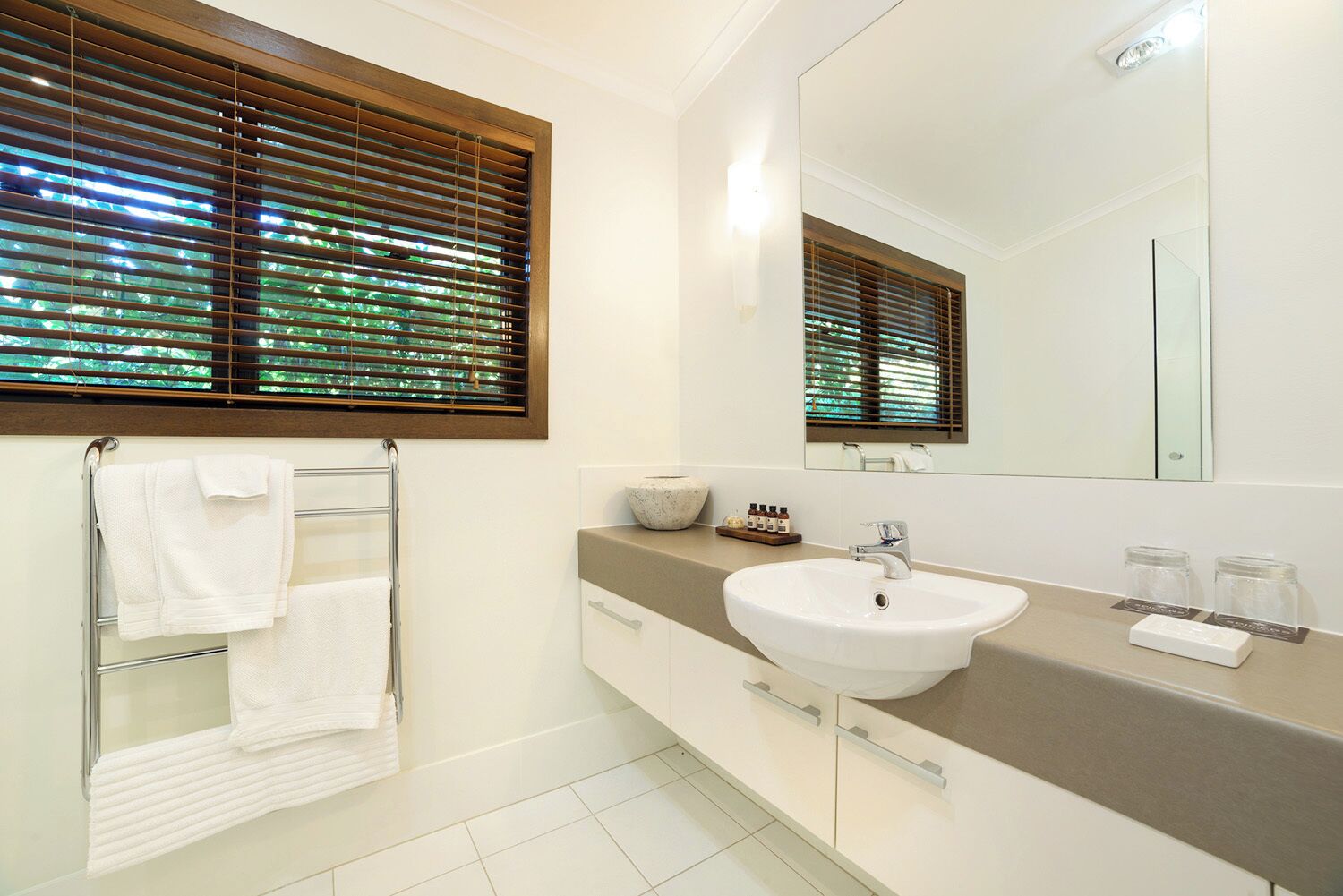 A modern bathroom with a white sink, a large mirror, and a towel rack.