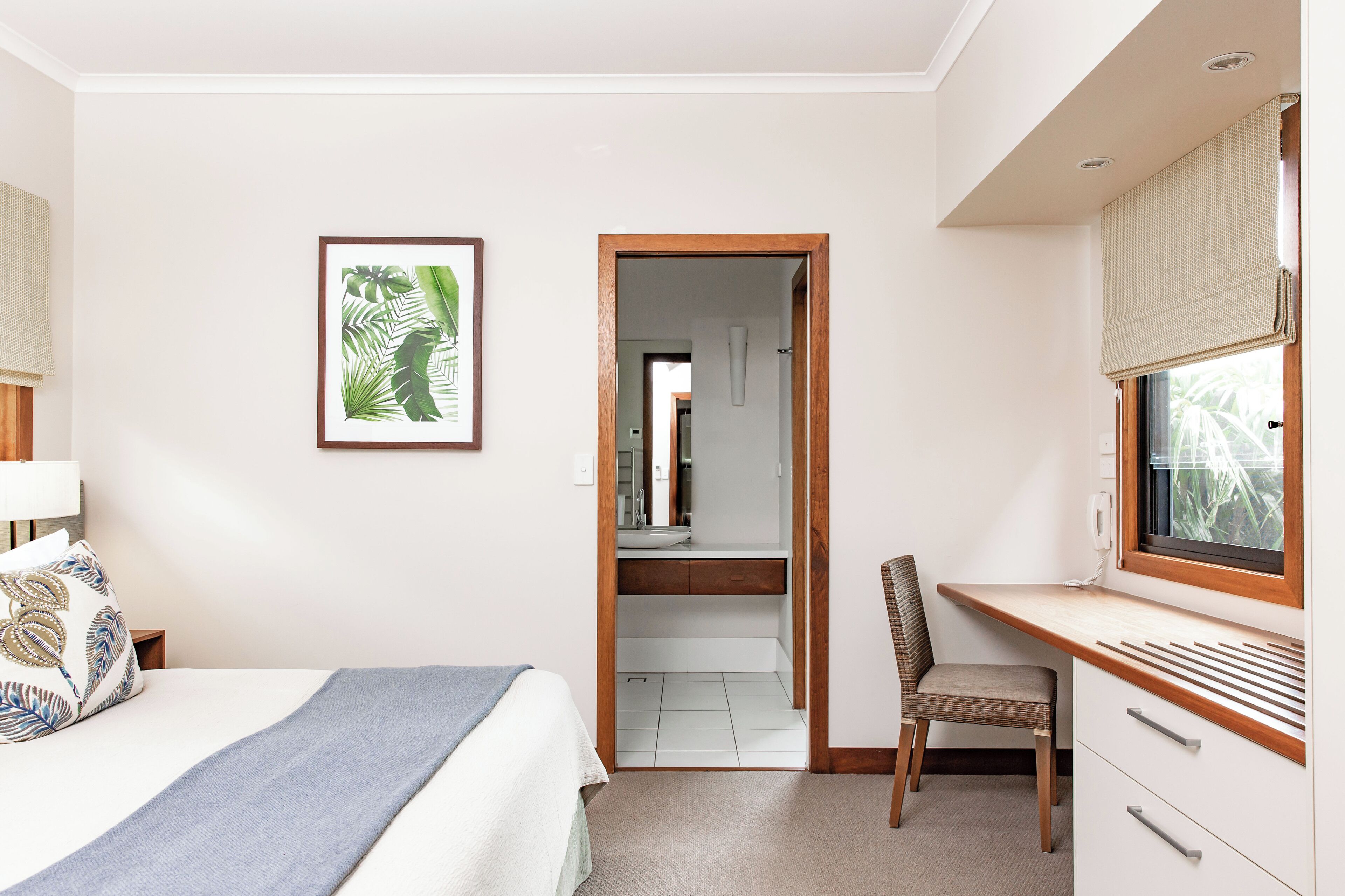 Une chambre d’hôtel avec un lit, un bureau et une chaise, une fenêtre donnant sur un paysage agréable et une salle de bain visible par une porte entrouverte.