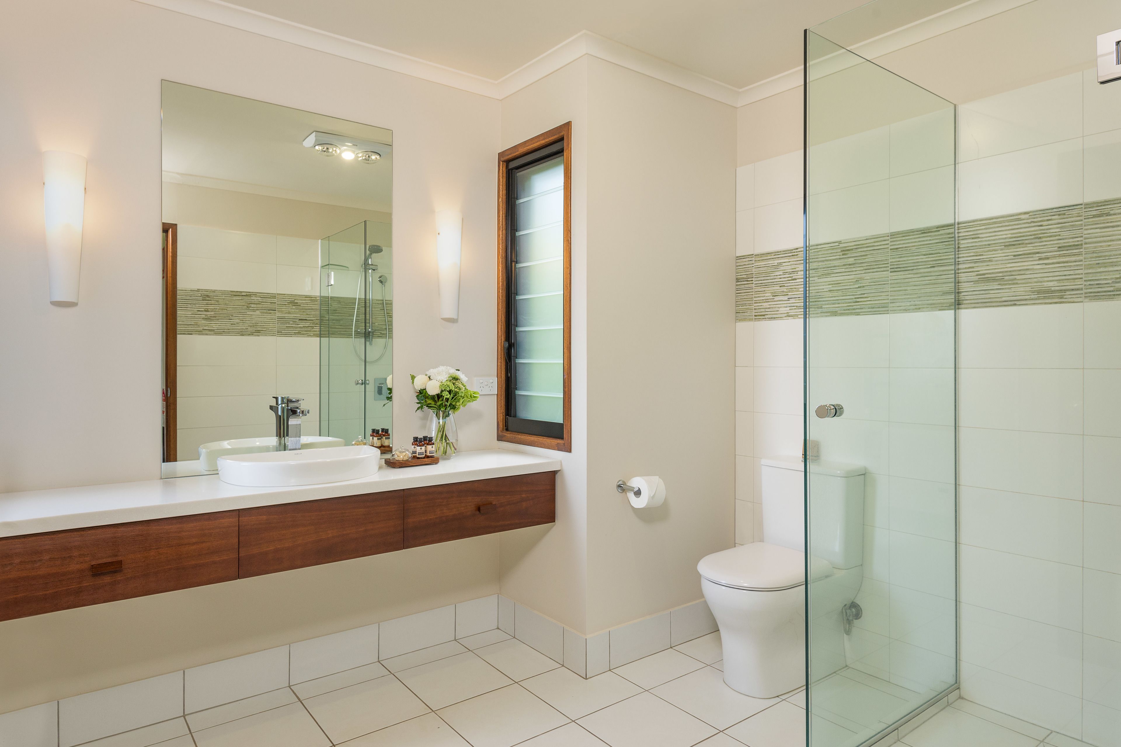A modern bathroom with a glass shower enclosure, a large mirror, and a white sink with a wooden vanity.