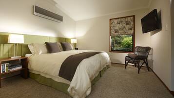 Habitación de hotel ordenada con una cama grande, una silla, un televisor y una ventana con vista a zonas verdes.