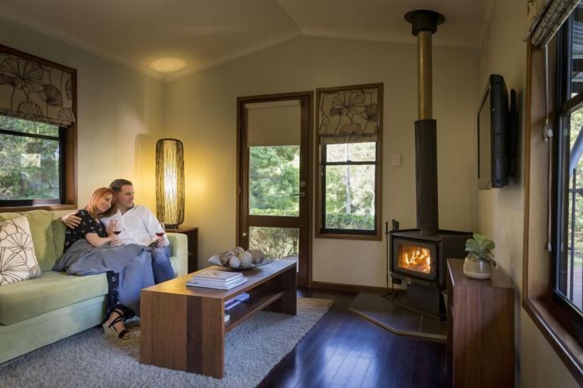 A cozy living room with a fireplace, a sofa, a coffee table, and a bookshelf.