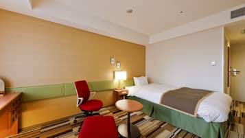 A hotel room with a bed, a desk, a chair, a small table, and a lamp.