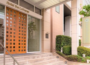 The entrance of Hotel the Lutheran with a wooden facade, a glass door, and a staircase leading up to the entrance. - Hotel the Lutheran (Osaka)