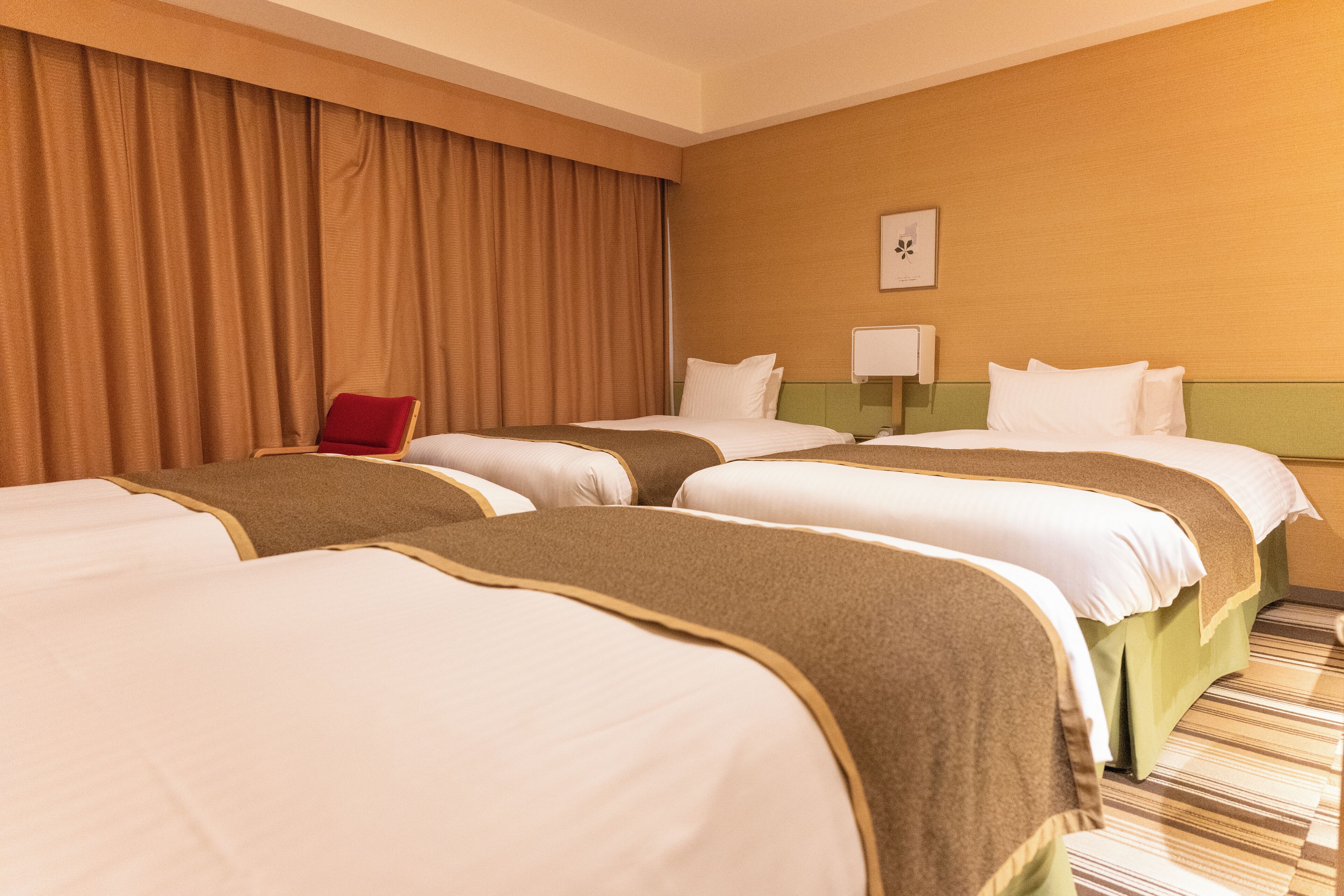 A hotel room with three beds, a red chair, and a wall-mounted lamp.