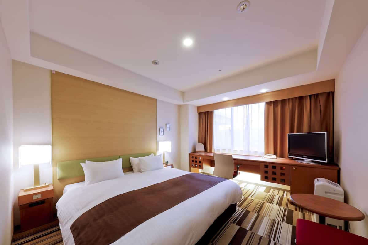 A hotel room with a large bed, a desk, a television, and a window with curtains.
