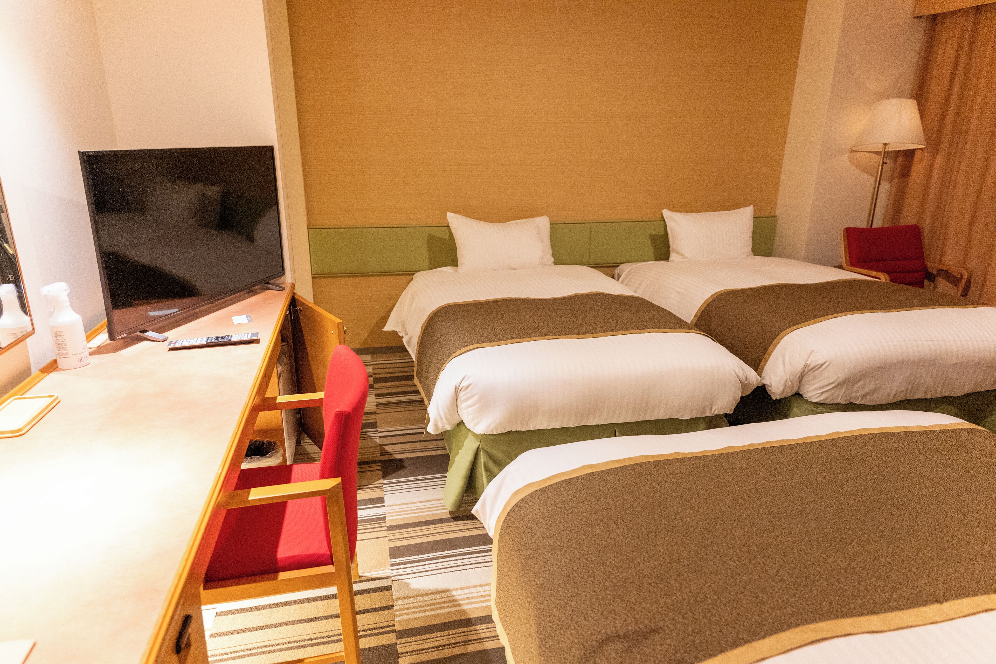 Ett hotellrum med två sängar, ett skrivbord, en tv och en röd stol.