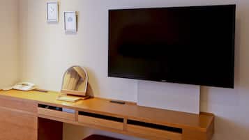 Een hotelkamer met een houten bureau, een flatscreen televisie, een telefoon, een spiegel en een rode gestoffeerde kruk.