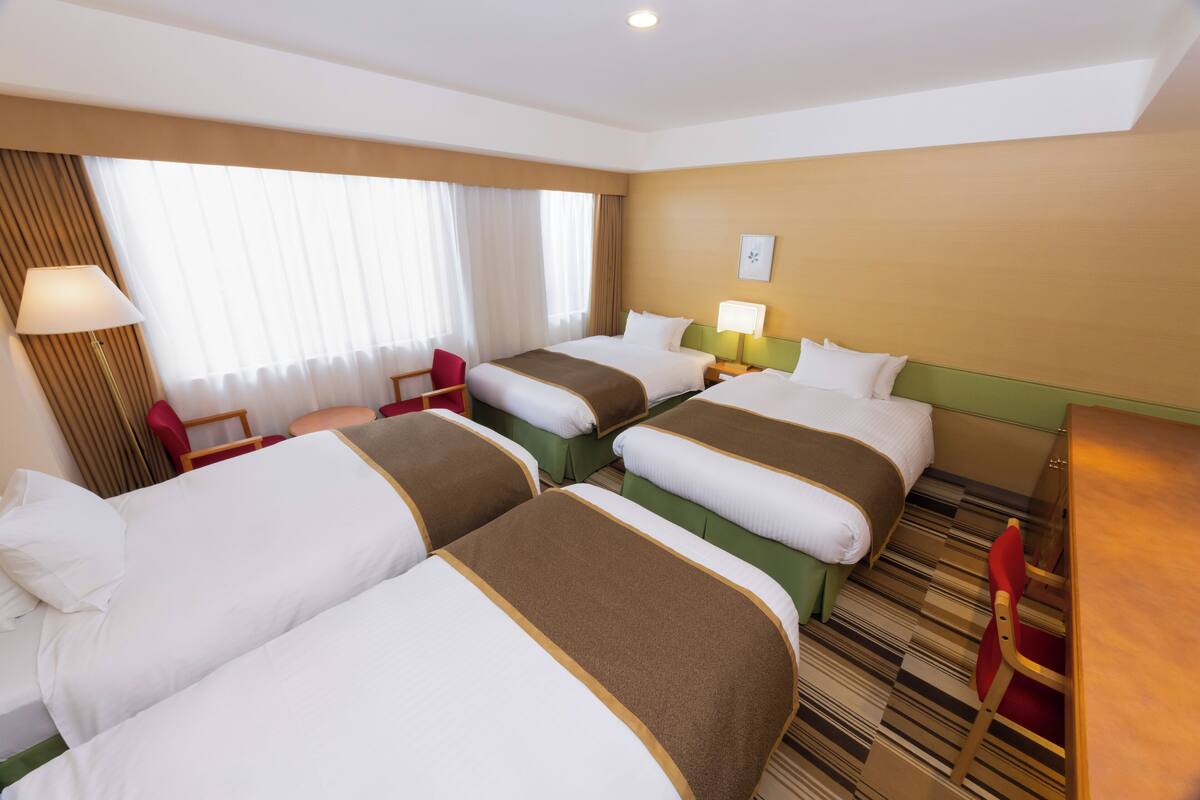 A hotel room with three beds, a desk, and a chair.