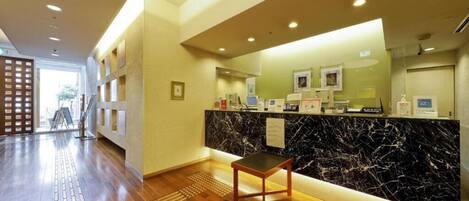 A hotel reception area with a marble counter, a wooden chair, and a clear view of the entrance.