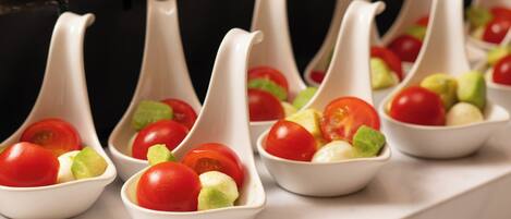 A series of white, spoon-shaped bowls containing cherry tomatoes and avocado slices.