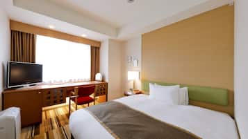 Ein Hotelzimmer mit einem Bett, einem Schreibtisch mit Fernseher, einem Sessel, einer Lampe und einem Fenster mit Vorhängen.