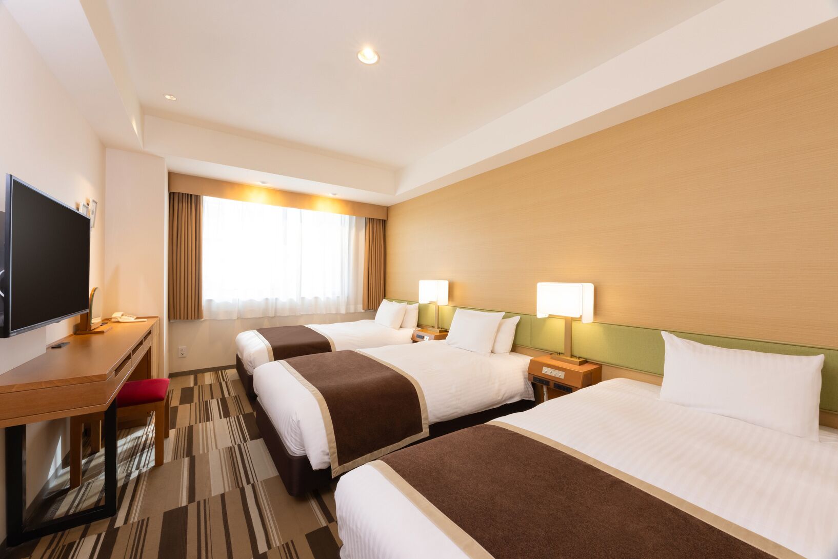 Habitación de hotel con dos camas, un escritorio, televisión y un ventanal con cortinas.