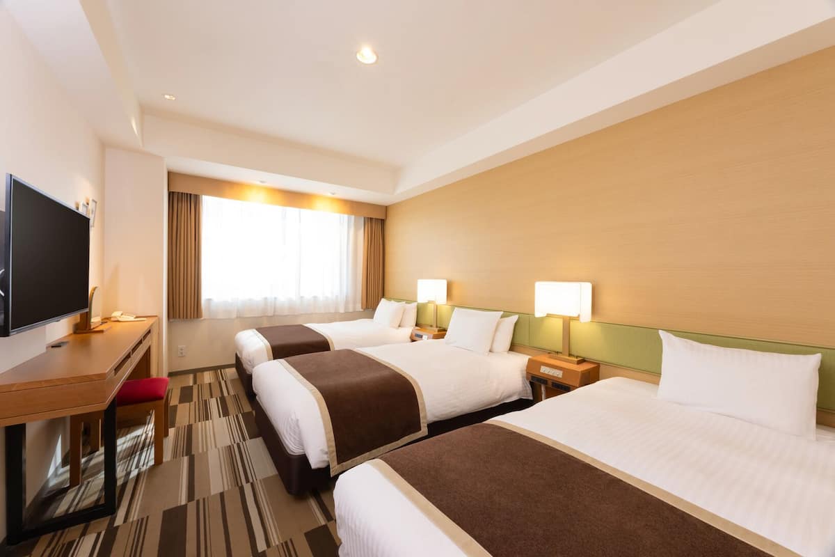 A hotel room with two beds, a desk, a television, and a large window with curtains.