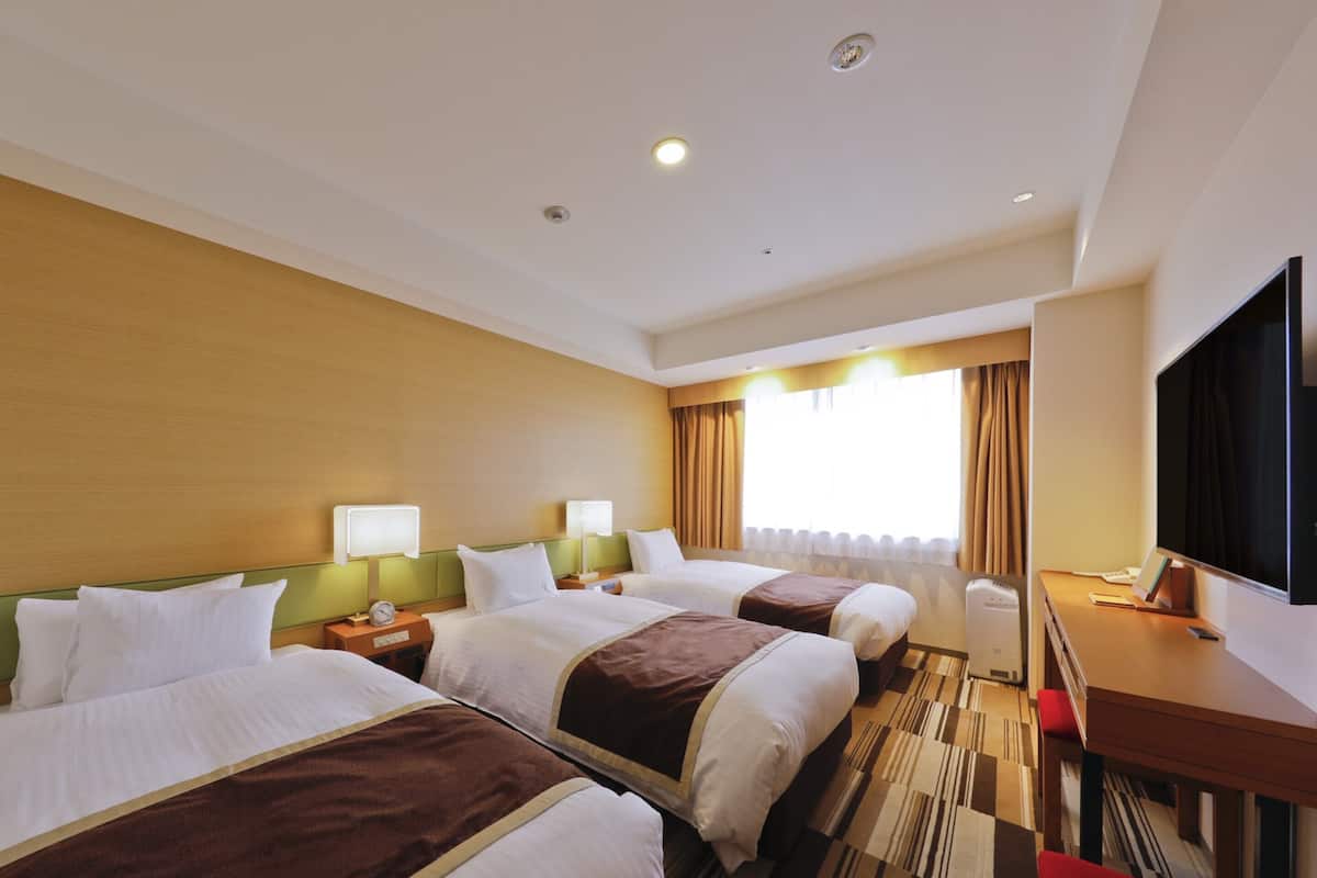 A hotel room with two beds, a desk, a TV, and a window with curtains.