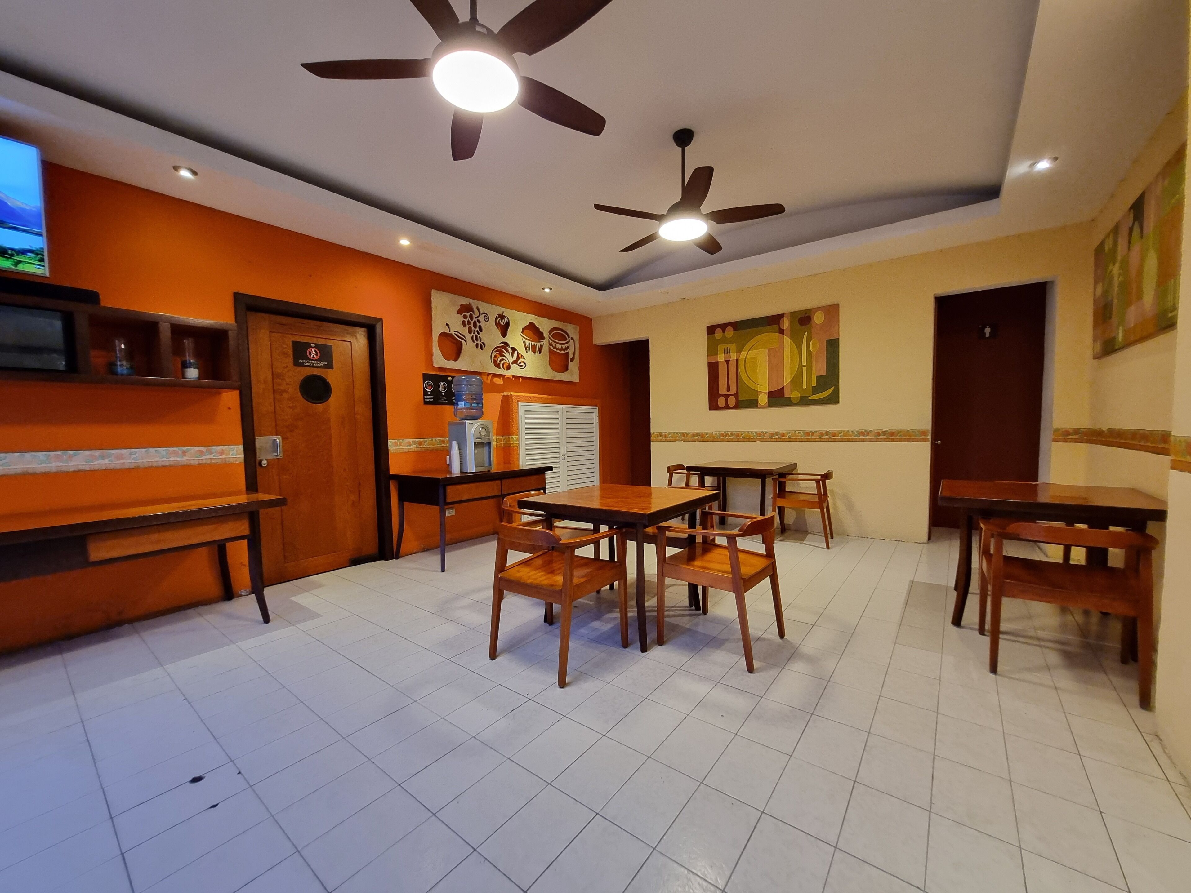 Restaurante com mesas e cadeiras de madeira, ventiladores de teto e chão de azulejos.