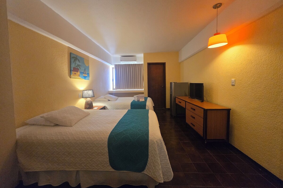 Habitación de hotel con dos camas, un escritorio, televisor, refrigerador y un cuadro en la pared.