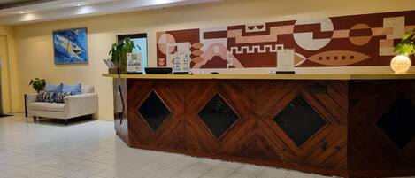 A reception desk with a wooden finish and geometric patterns, a sofa with patterned cushions, and a painting on the wall.