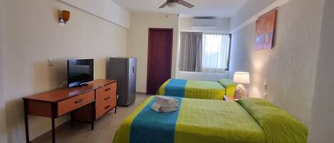 Una habitación de hotel con cama, escritorio, televisor y ventilador de techo.
