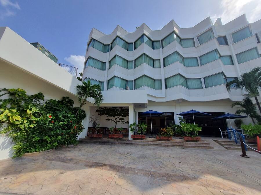 A modern multi-story hotel with a zigzag facade, outdoor seating area with umbrellas, and potted plants.