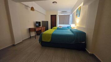 A hotel room with a bed, a desk with a television, a wardrobe, and a window with curtains.