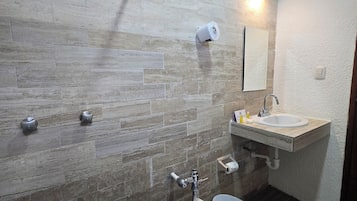 A modern bathroom with a stone wall, a toilet, a sink, and a shower.