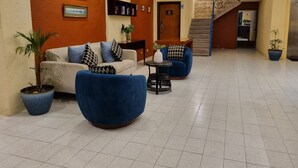 A lobby with a sofa, armchairs, a small table, potted plants, a staircase, and framed certificates on the wall. - Hotel Plaza Cozumel (Cozumel)
