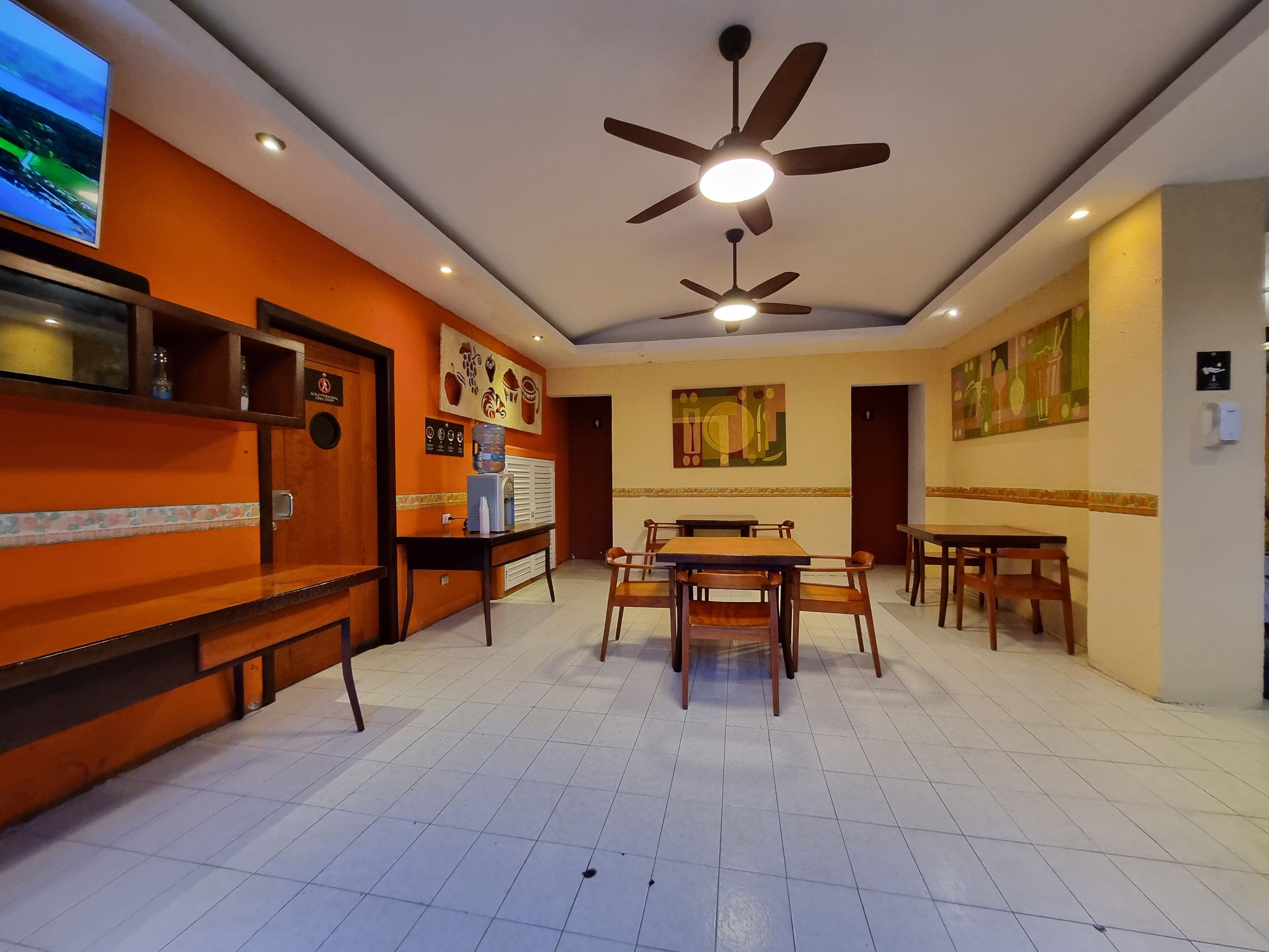 A hotel lobby with a reception desk, seating area, ceiling fans, and artwork on the walls.