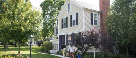 A two-story house with a brick chimney, a front porch, and a well-maintained lawn.
