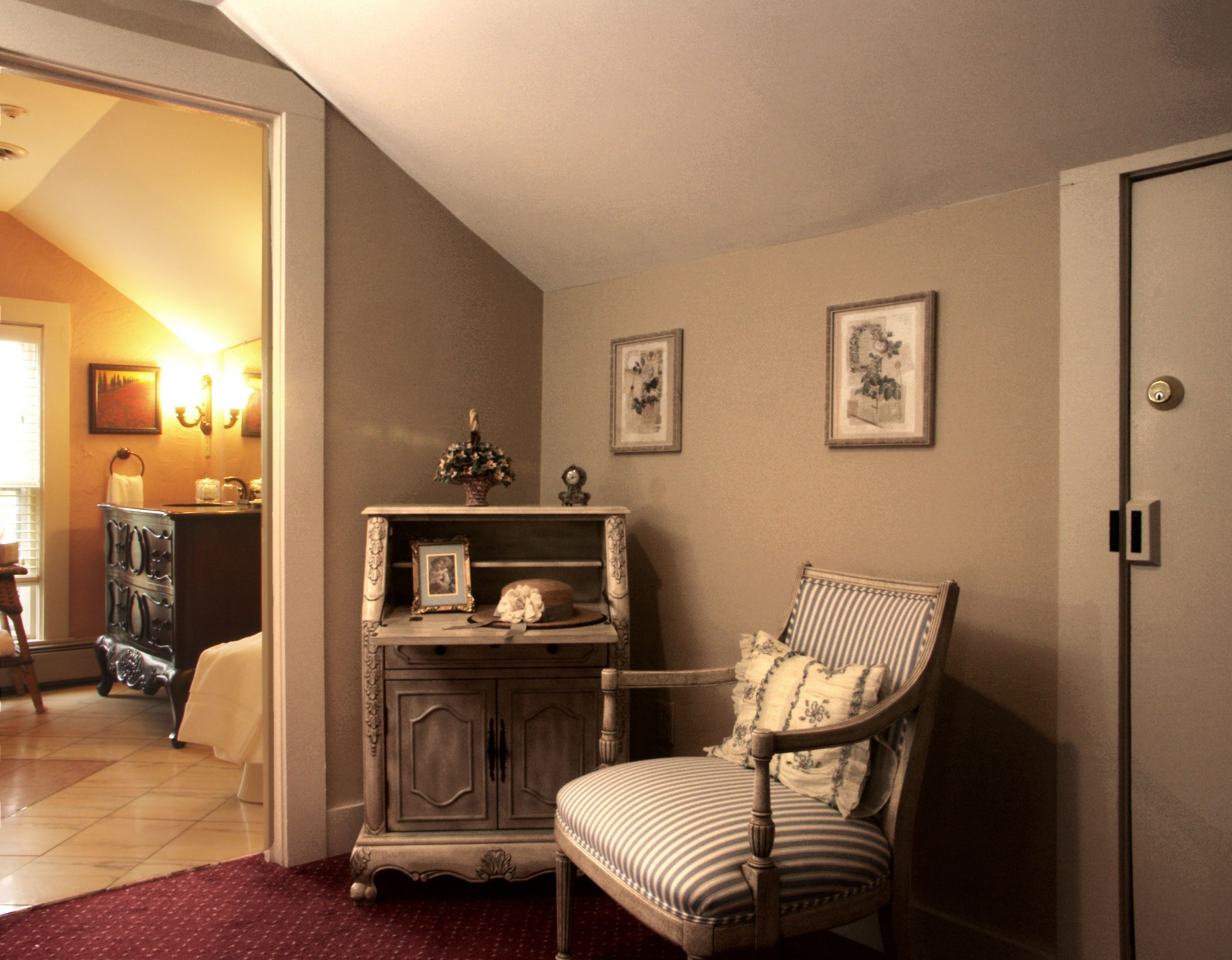 A room with a vintage-style dresser, a striped armchair, and two framed pictures on the wall.