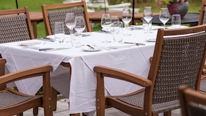 An outdoor dining area with a table set for six, surrounded by wicker chairs, in a garden setting with hanging planters and a lamp post. - The Reluctant Panther Inn and Restaurant (Manchester)