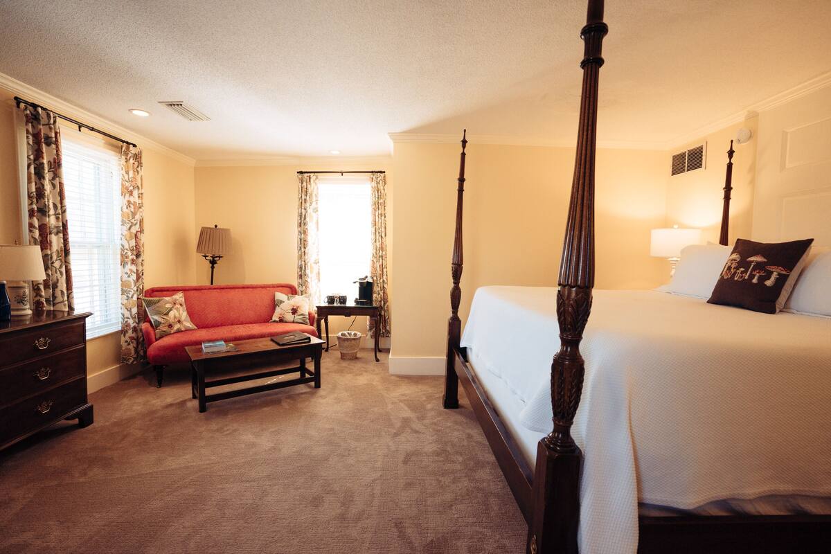 Ein Himmelbett, ein rotes Sofa, eine Holzkommode und eine Lampe im Hotelzimmer.