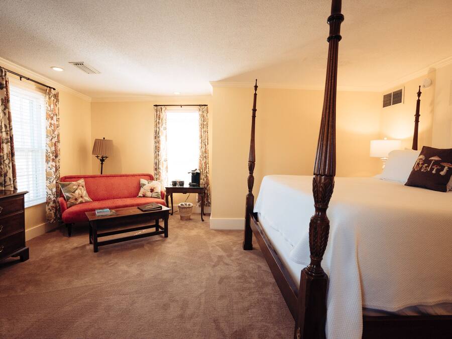 A four-poster bed, a red sofa, a wooden dresser, and a lamp in a hotel room.