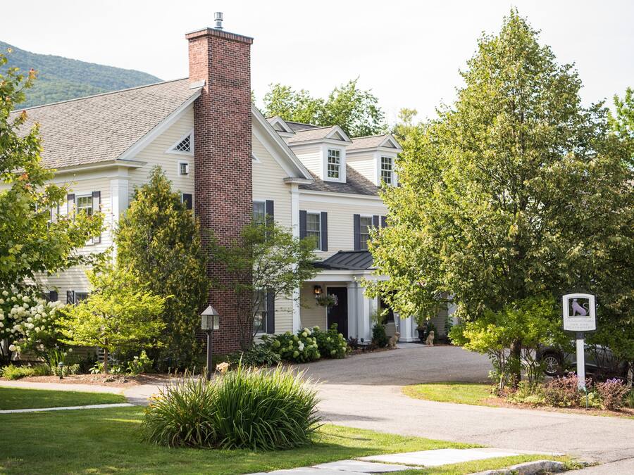 A large, two-story house with a brick chimney, surrounded by lush greenery and a well-maintained lawn.