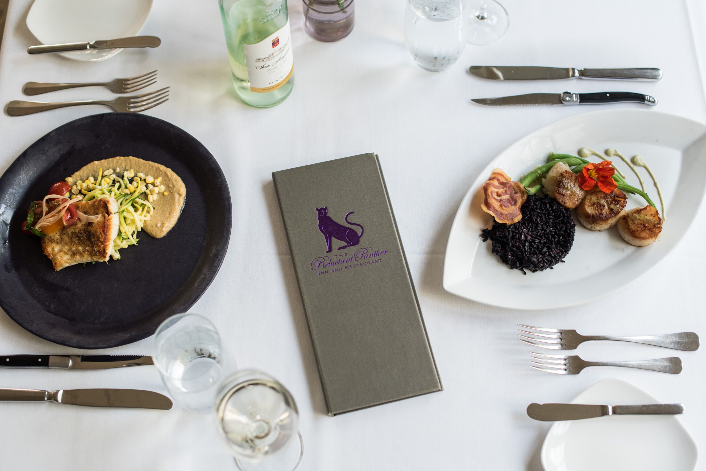 A dining table set with plates of food, cutlery, and a menu.