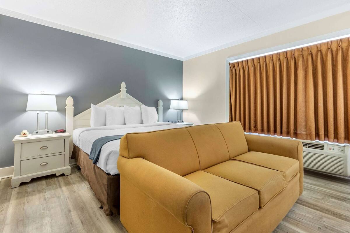 Una habitación de hotel con una cama, dos mesitas de noche con lámparas, un sofá y una ventana con cortinas.